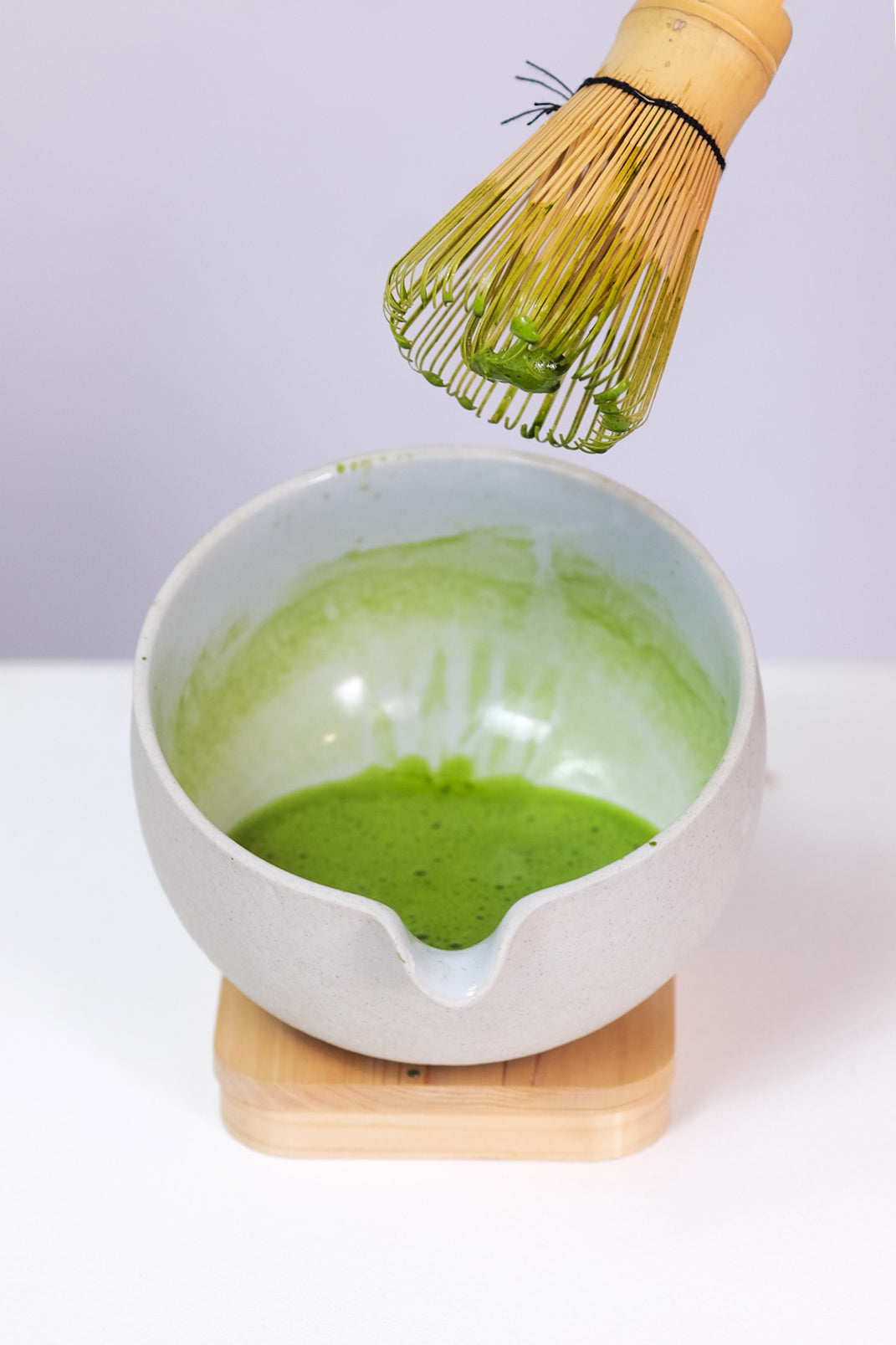 White bowl with green tea mixture and a whisk on a white background