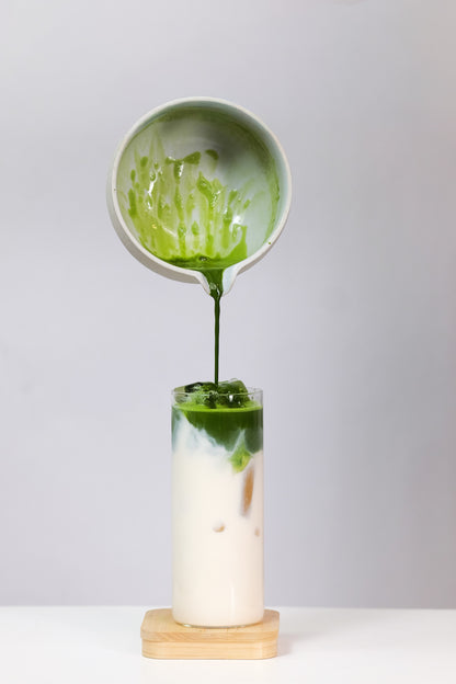 Matcha being poured from a small bowl into a glass with a white background
